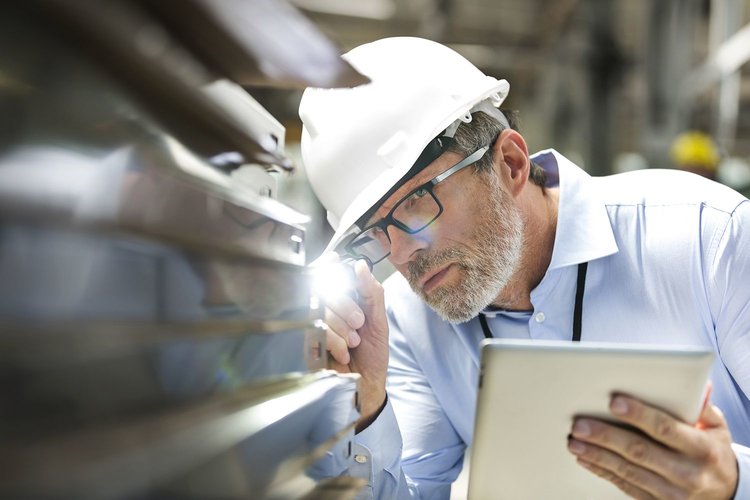 Un hombre con casco inspeccionando la calidad de una fábrica usando una tableta