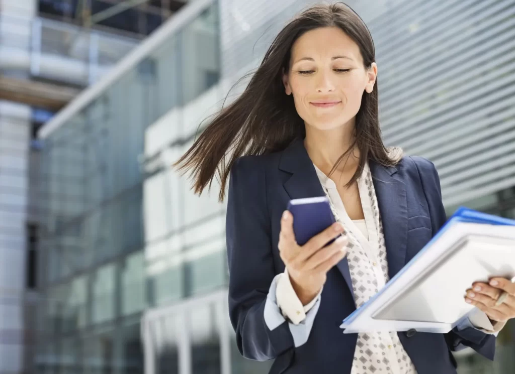 Una mujer de negocios sostiene una carpeta mientras administra documentos en su teléfono celular.